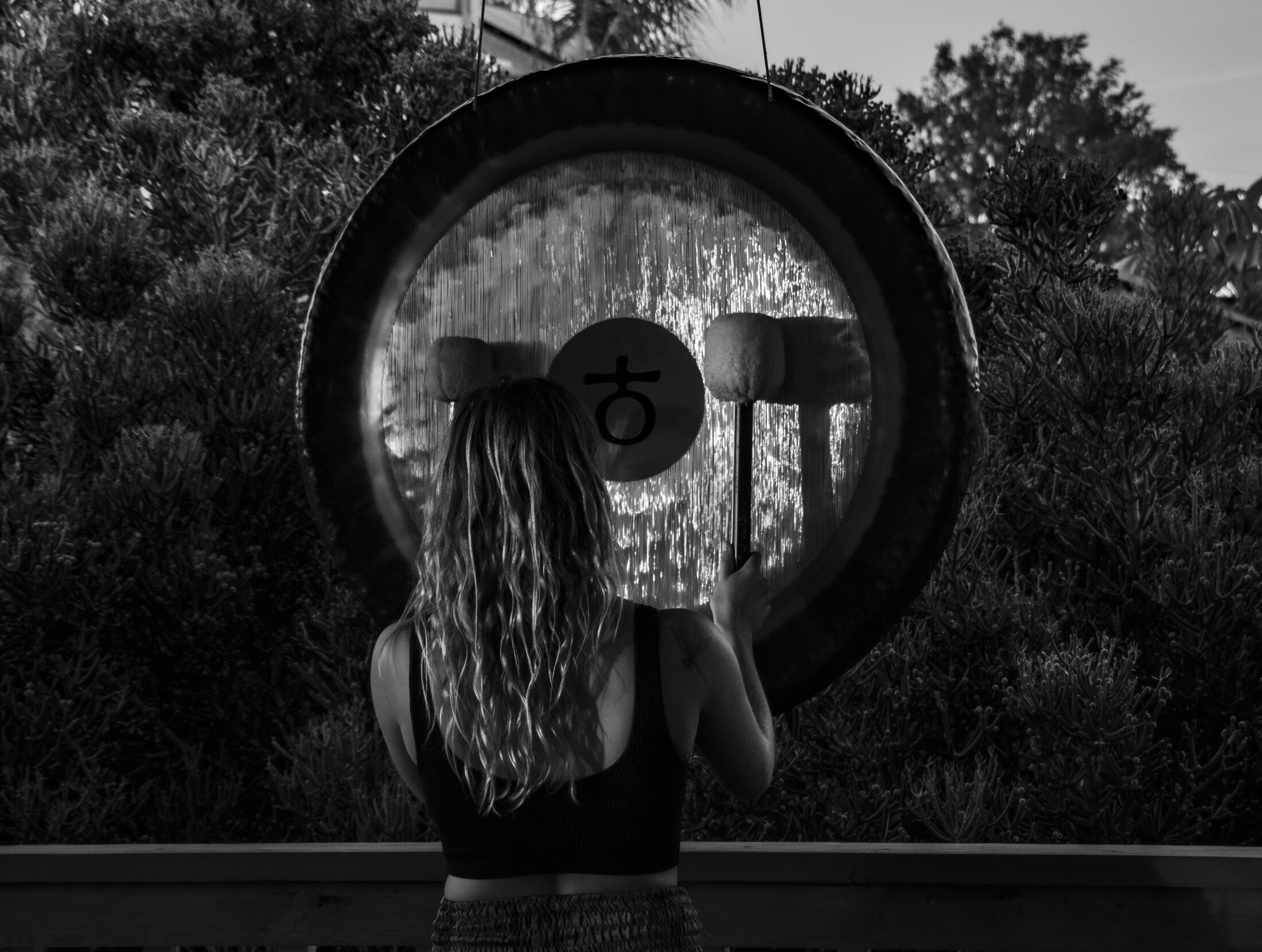 Riley sounding a large gong outdoors at dusk.