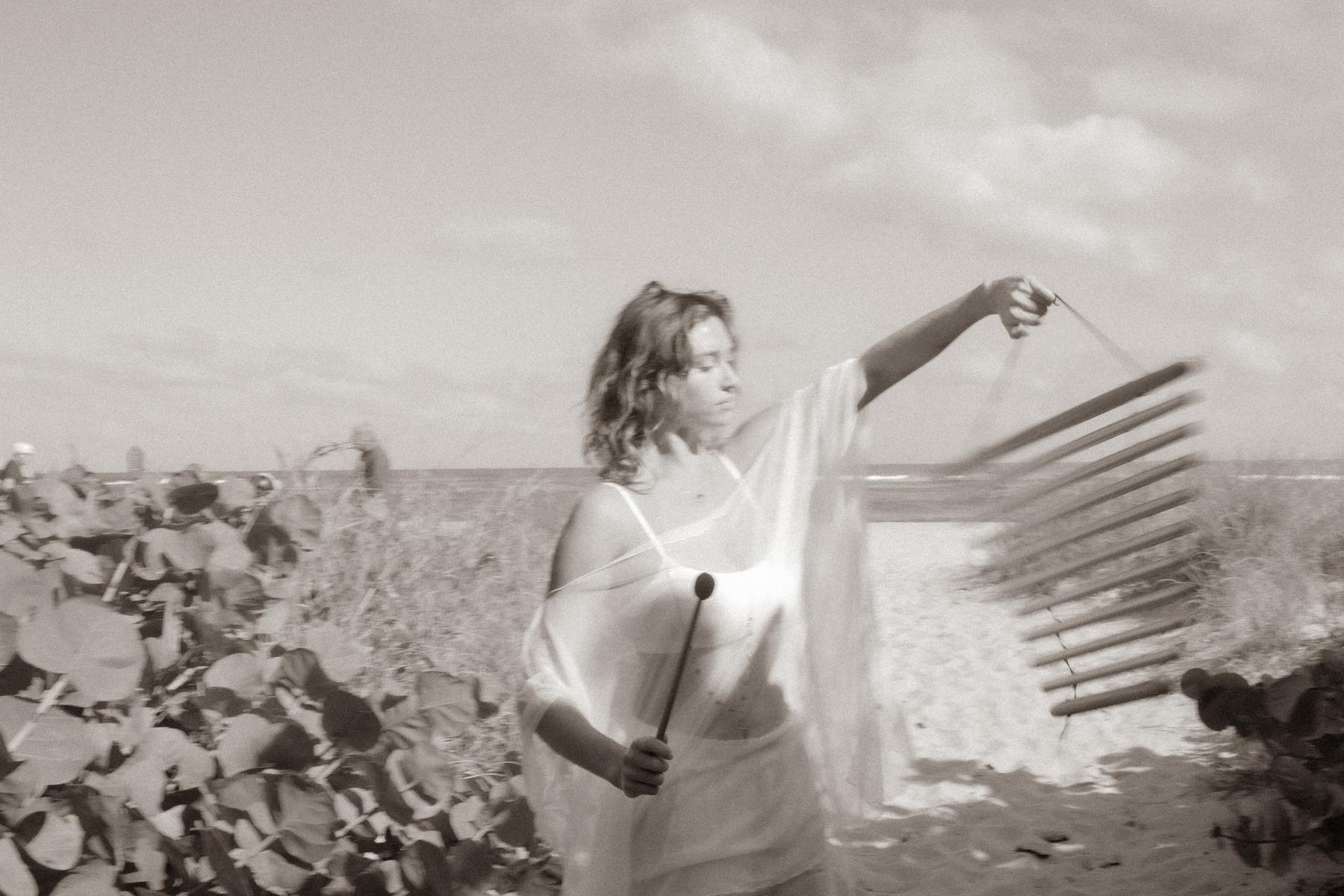 Riley on the shoreline sounding a wind chime, bowls set out among the sea grape leaves.